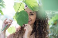 Giovane donna sorridente con grande foglia verde in primo piano, sfondo verde bokeh
