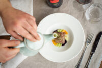 Mani di chef che decorano un piatto gourmet bianco con salse e ingredienti, cucina d'autore