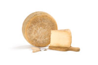 Forma intera e fetta di formaggio stagionato su superficie chiara, fotografia di prodotto lattiero-caseario