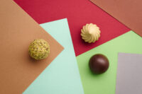 Praline di cioccolato artigianali su sfondo geometrico con forme colorate rosse, verdi e beige
