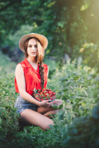 Giovane donna con cappello rosso seduta all'aperto tra la vegetazione, atmosfera estiva