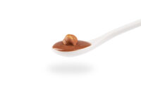 Cucchiaio bianco con crema alla nocciola su sfondo bianco, fotografia minimalista di prodotto dolciario