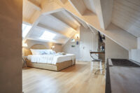 Camera in mansarda luminosa con letto bianco, soffitto inclinato in legno e finestra velux