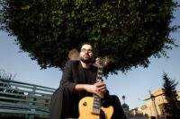Musicista con chitarra elettrica in posa, sfondo scuro, atmosfera artistica