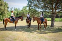 Persone a cavallo in un campo aperto con alberi sullo sfondo