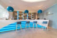 Bar lounge moderno con bancone illuminato in blu, sgabelli alti e lampade pendenti blu
