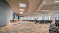 Sala conferenze moderna con file di sedie, palco e lucernari sul soffitto