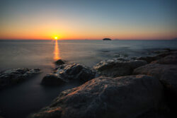 Tramonto sul mare con rocce in primo piano e cielo dai colori arancione e blu intenso
