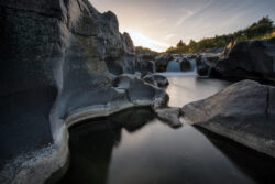 Paesaggio naturale con fiume tra le rocce al tramonto, luce calda e riflessioni sull'acqua