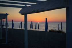 Tramonto sul mare con gazebo e ombrelloni in silhouette, cielo arancione e viola